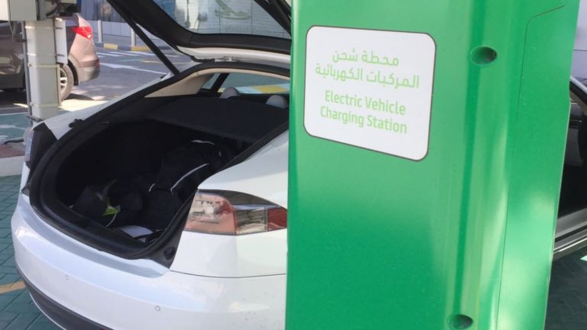 A white electric car charging at a green Electric Vehicle Charging Station in the UAE